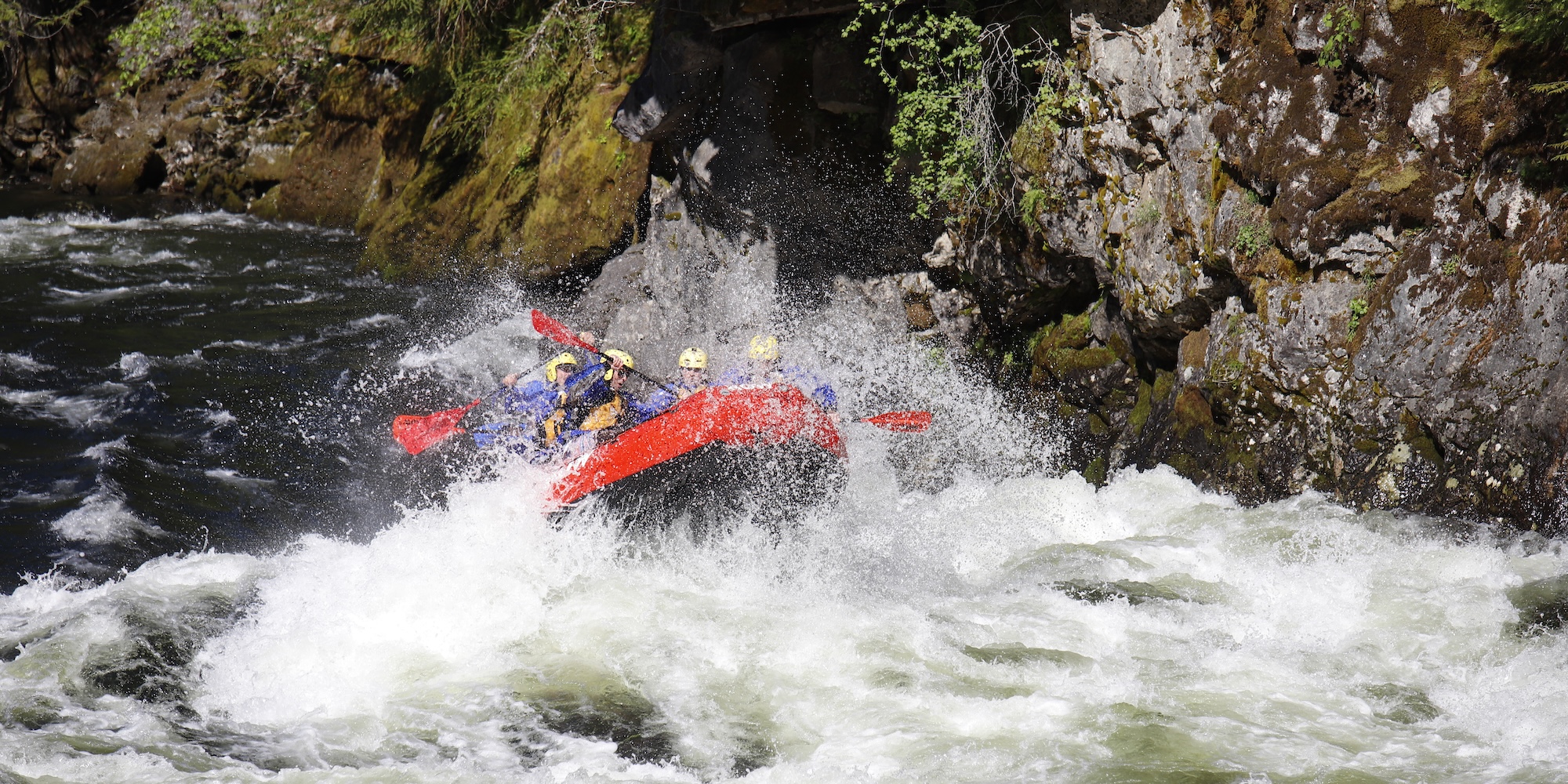 Raft crashing through a large wave on the Lochsa River, surrounded by mossy cliffs and dense forest.