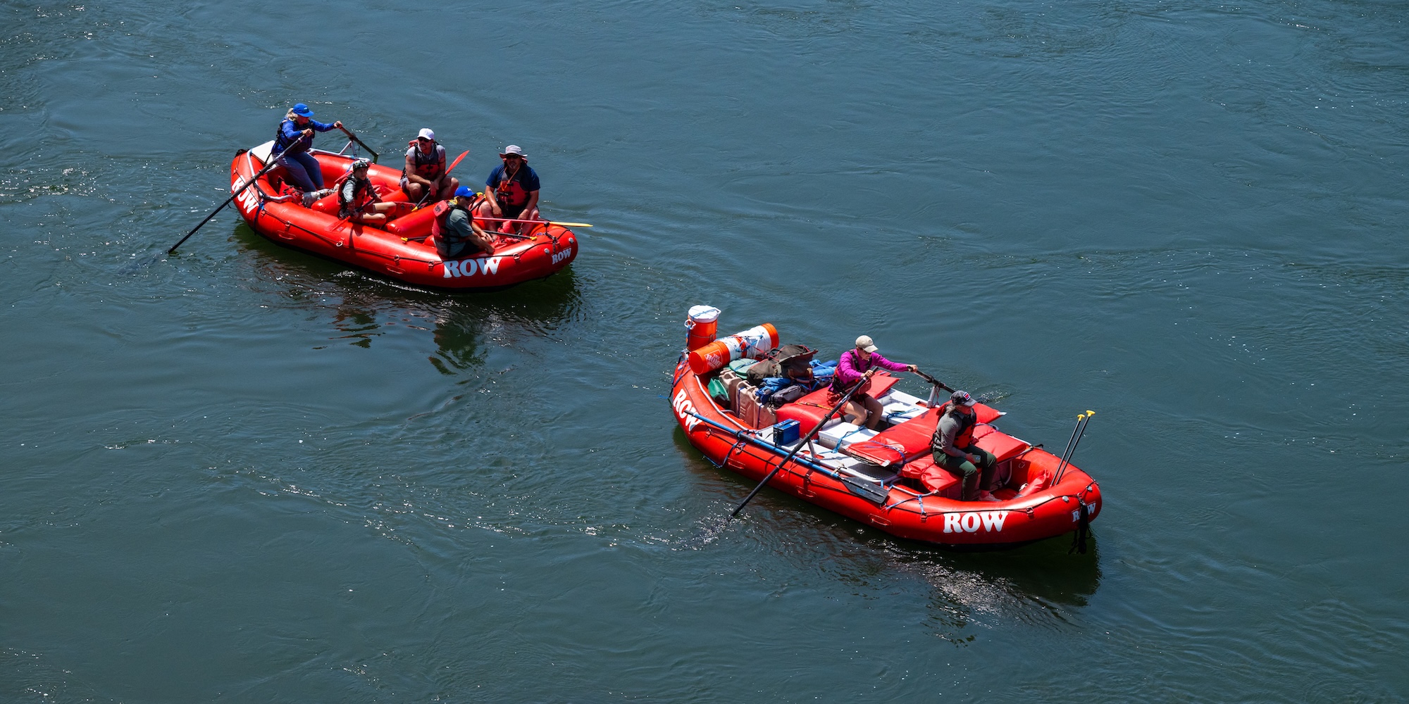 Two fully loaded gear boats float downriver, carrying supplies and guided rafters during a multi-day whitewater rafting trip.
