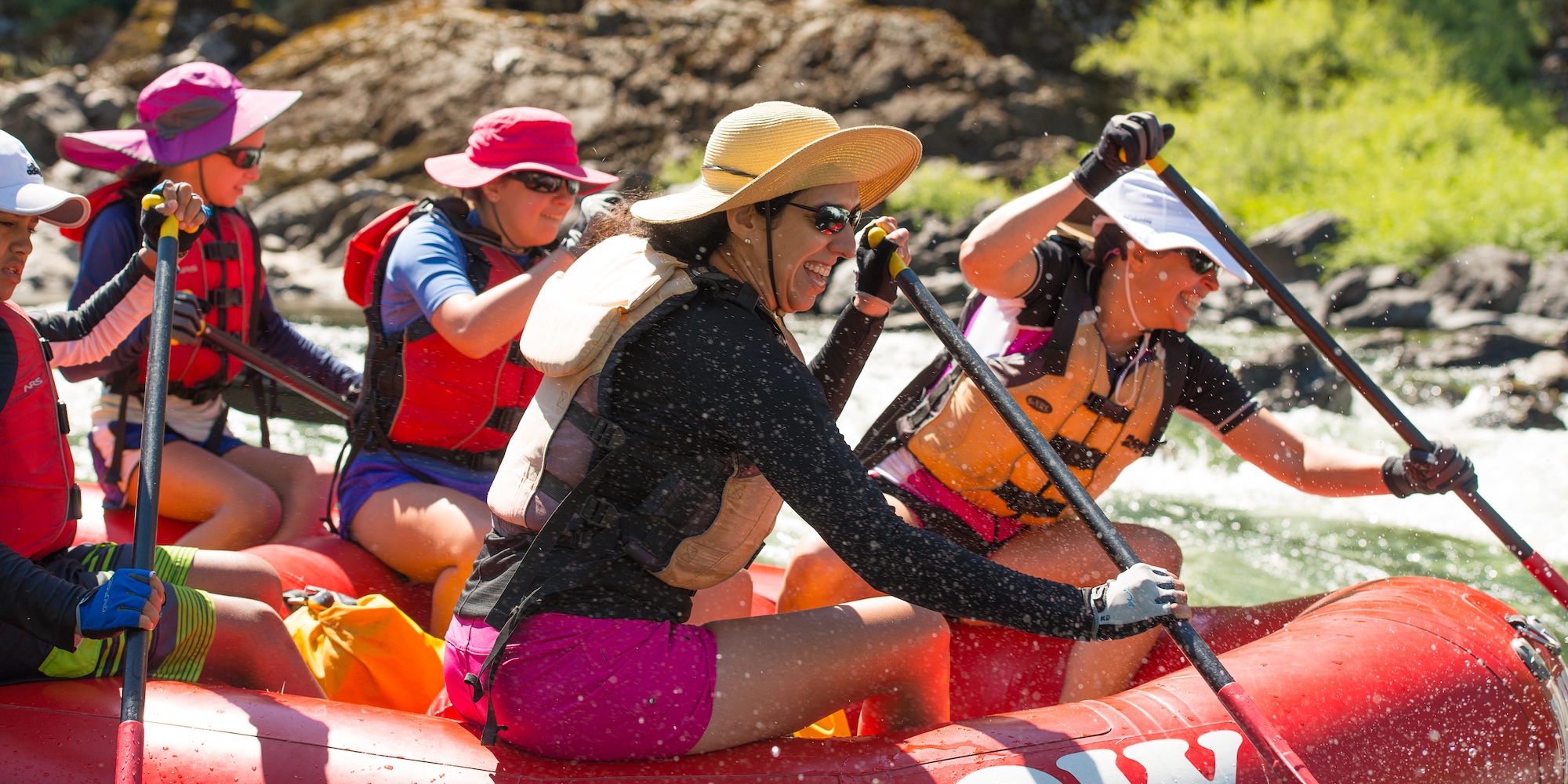 Close-up of happy rafters in sun hats and gear paddling together, dressed for warm-weather rafting conditions.