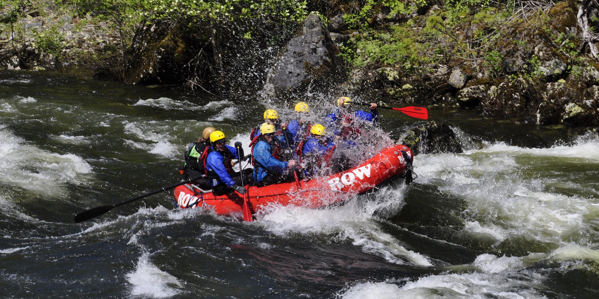 A red ROW Adventure Center raft with guests rafting down a splashy section of the Lochsa river. 