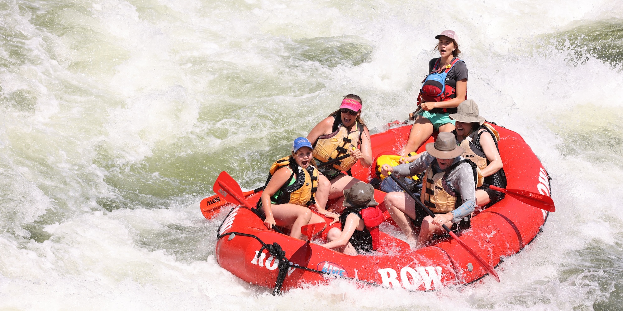 Family rafting through a large wave with water splashing around the boat.