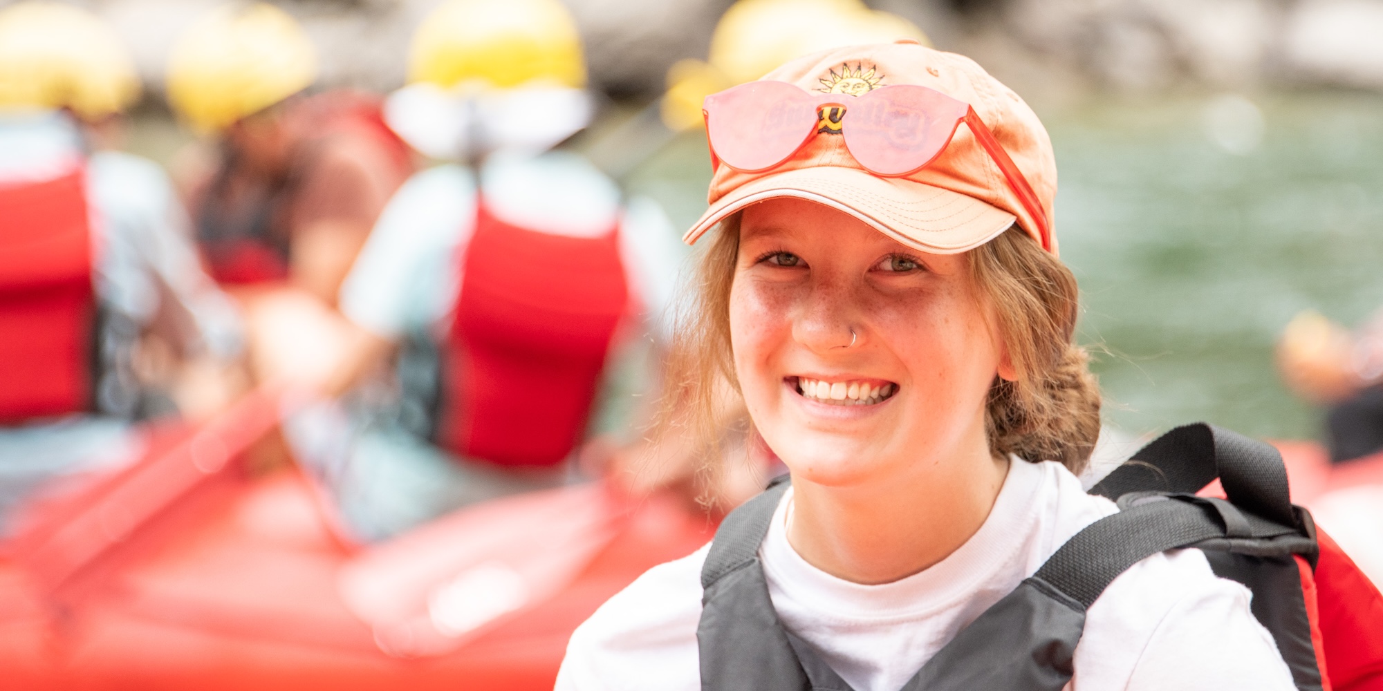 Smiling guest wearing a life jacket sits in a raft on the river before launching.