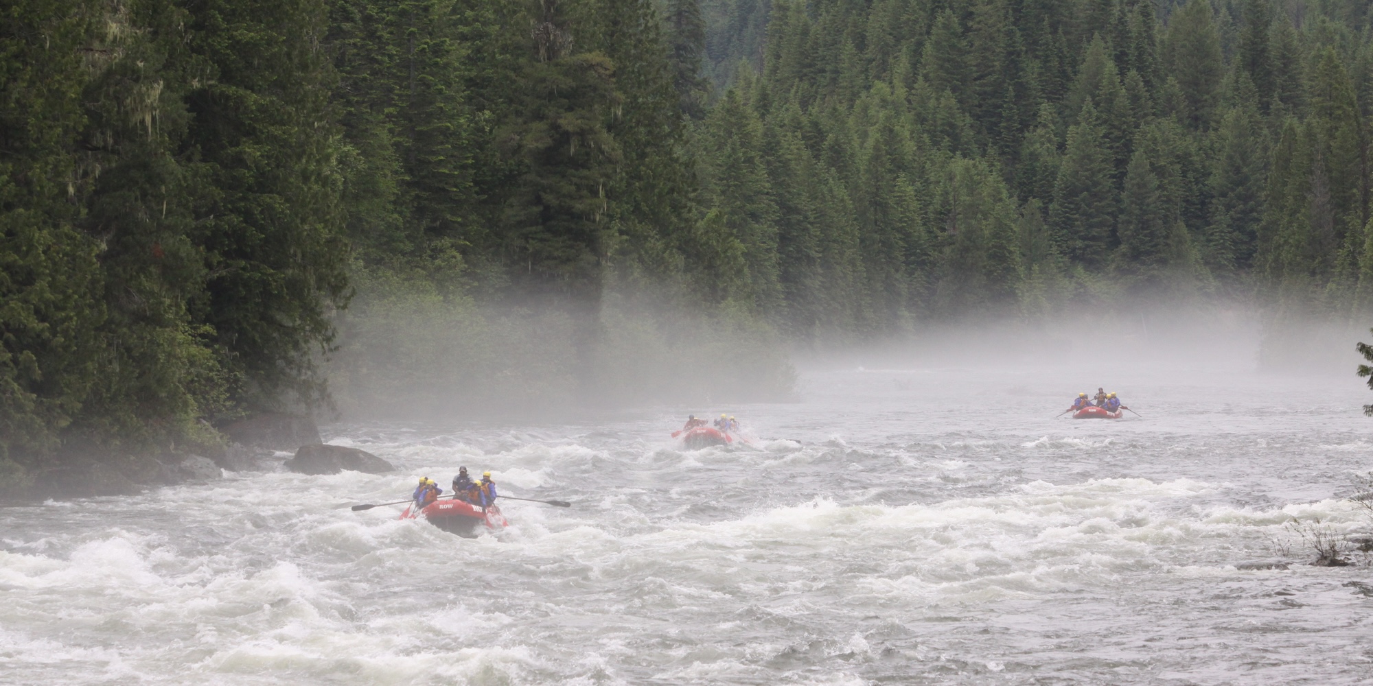 A group of red rafts navigating down the Lochsa river on a misty day.