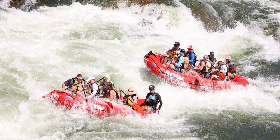 Two red ROW Adventures rafts paddling through a rapid section of the Clark Fork river in Montana. 