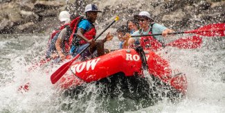 Group paddling through splashy whitewater rapids in a red raft.