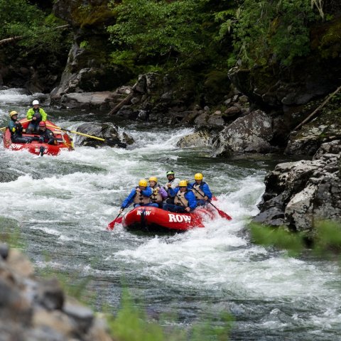 Two red rafts making their way through a scenic canyon on the St. Joe River, surrounded by rocky walls and lush forest.